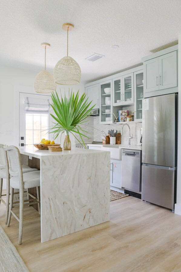 A modern kitchen with a marble island, white cabinets, stainless steel appliances, and a potted plant.