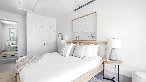 Un dormitorio moderno con una cama grande, dos mesitas de noche con lámparas, un espejo y una obra de arte enmarcada en la pared.