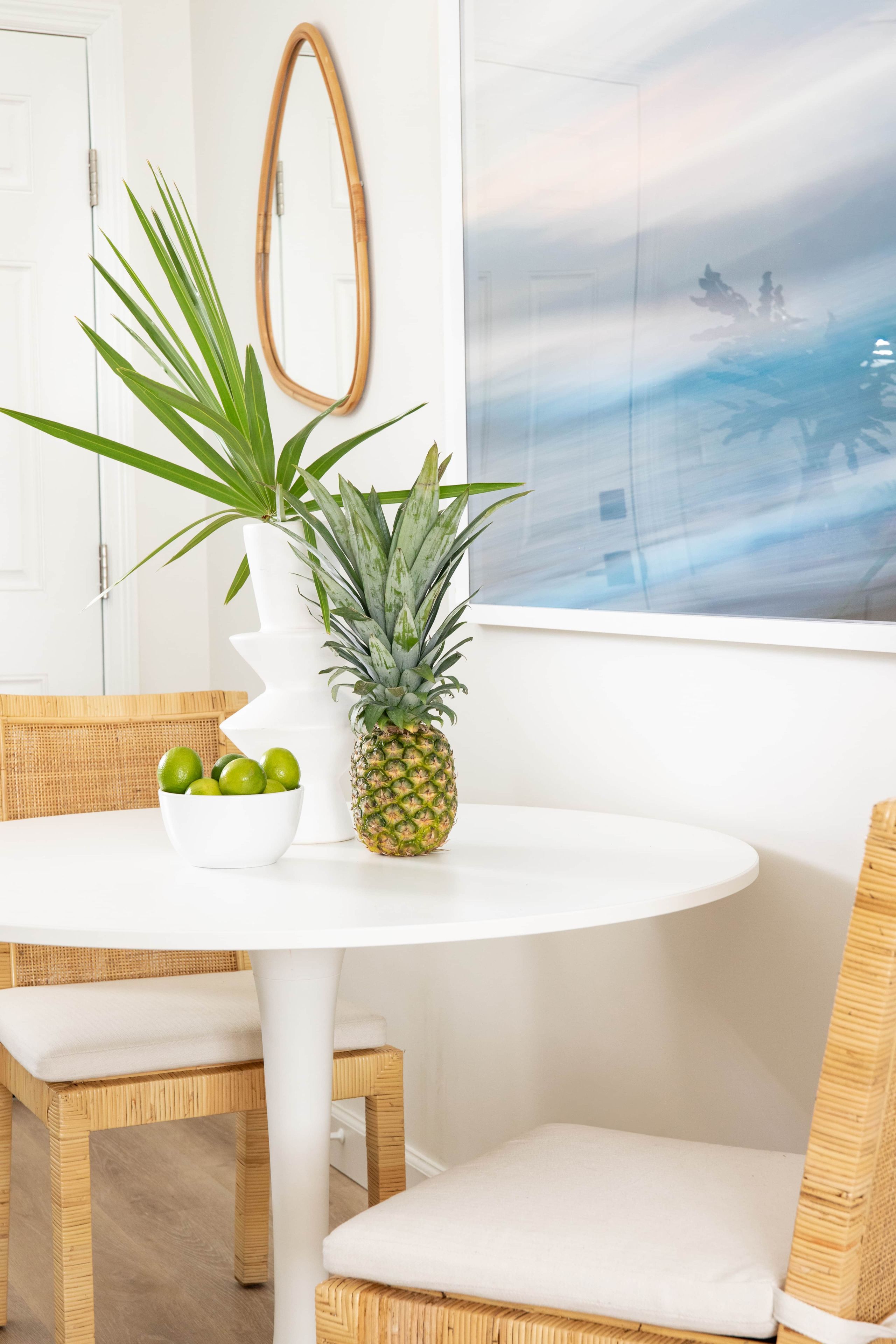A white round table with a pineapple, a bowl of limes, and a potted plant.