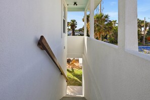 A narrow stairway leading to a balcony with a view of palm trees and a blue sky.