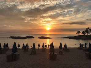 Una spiaggia con ombrelloni e tavoli, un tramonto e mare calmo.