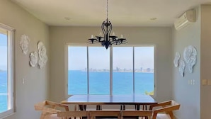 A dining area with a large table and chairs, a chandelier, and a view of the sea.