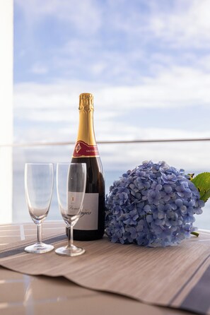 A bottle of wine, two glasses, and a cluster of blue hydrangeas on a table with a view of the sky. - Barracuda Hotel (Ponta Delgada)