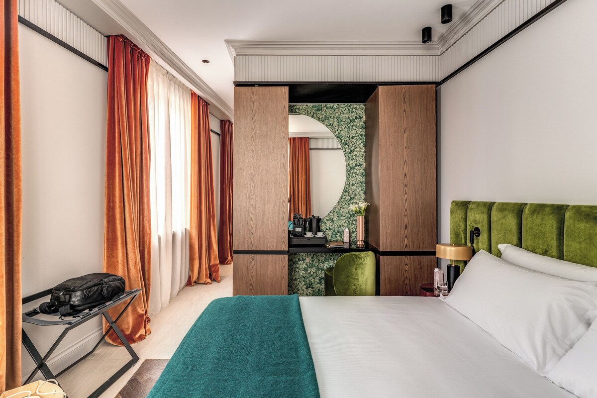 A hotel room with a bed, a desk, a chair, and a mirror.