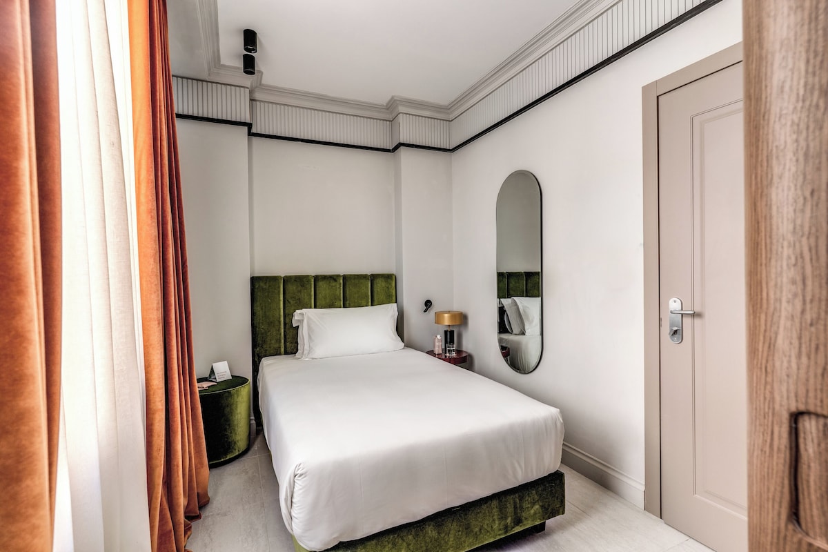 A hotel room with a bed, a bedside table, a mirror, and a door.