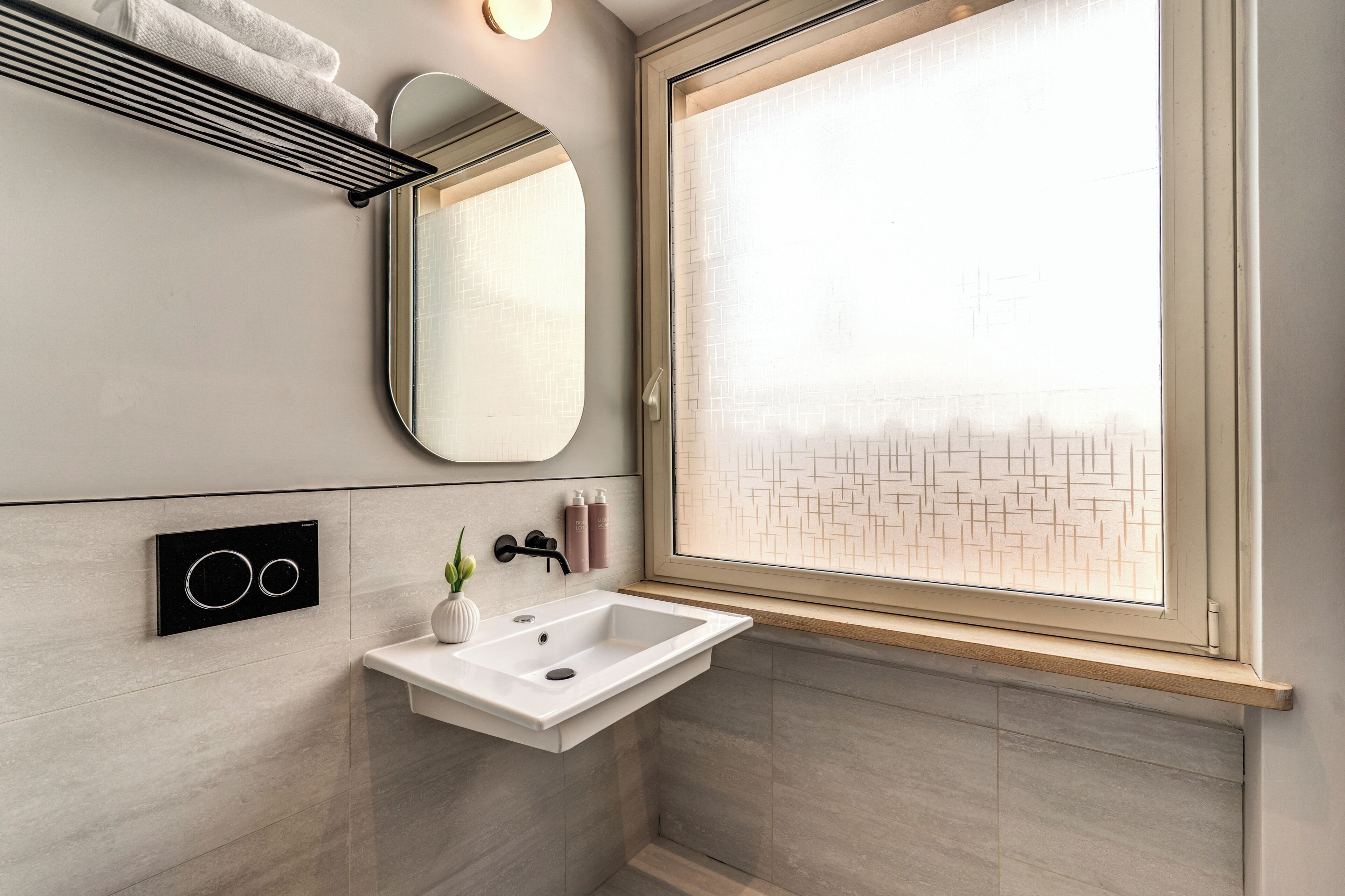 A bathroom with a white sink, a mirror, a towel rack, and a window with a geometric pattern.