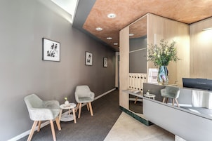 A reception area with a desk, chairs, framed artwork on the wall, and a vase with flowers.
