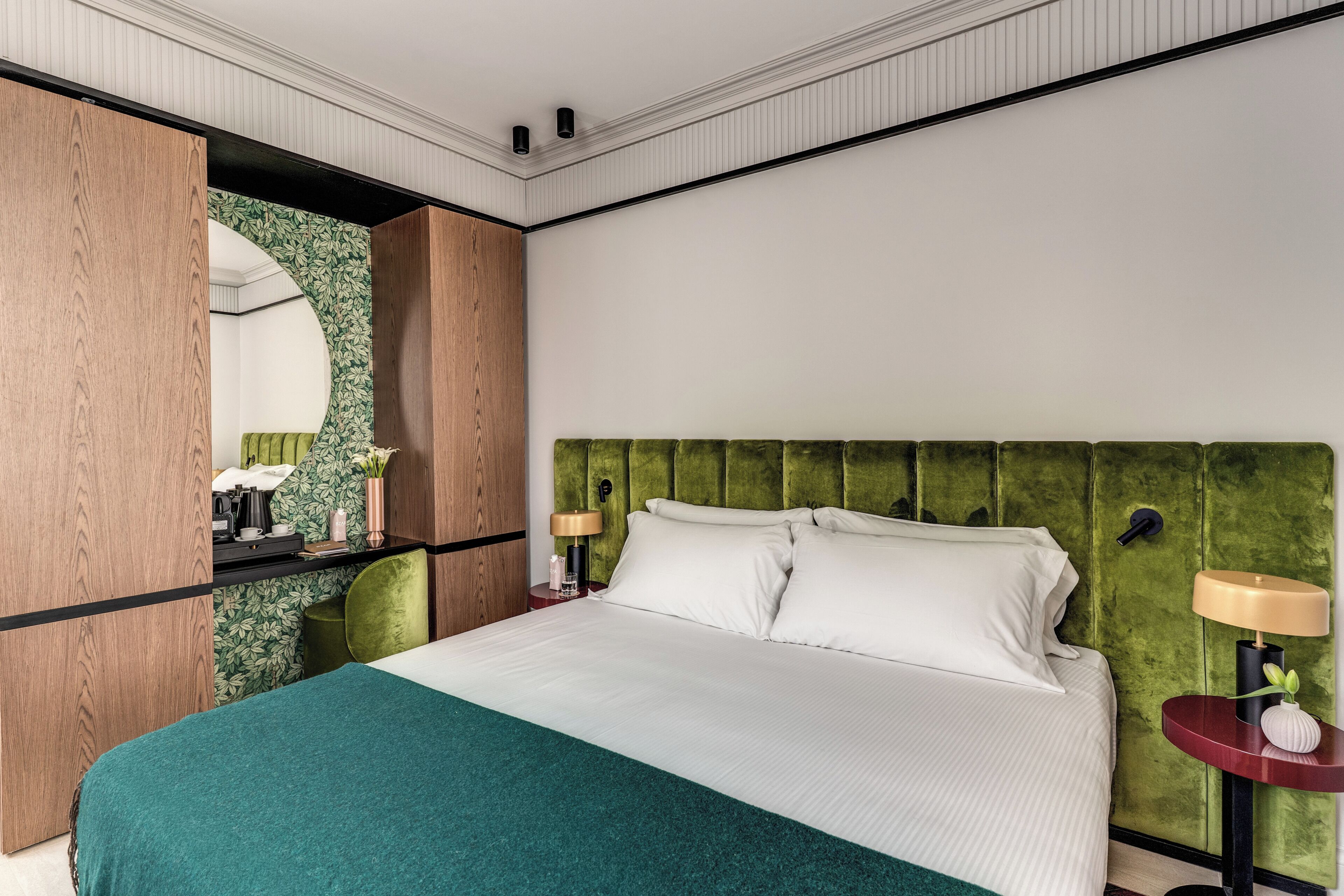 A hotel room with a bed, green headboard, bedside tables with lamps, a mirror, and a green accent wall.