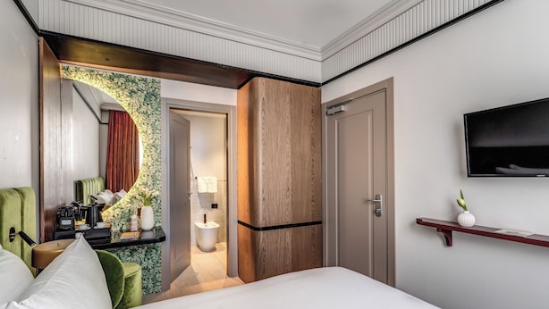 A hotel room with a bed, a desk with a lamp, a television, and a bathroom visible through an archway. - Hotel Santa Maria Maggiore (Rome)