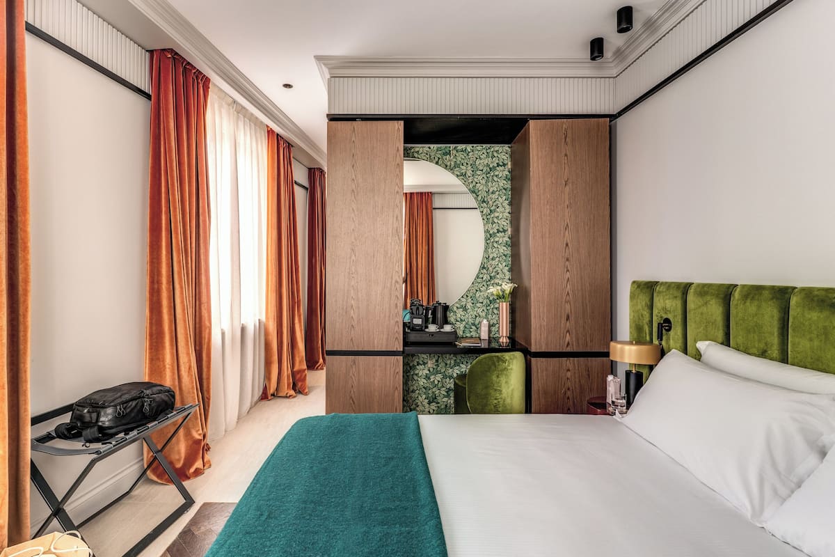 A hotel room with a bed, a desk, a chair, and a mirror.