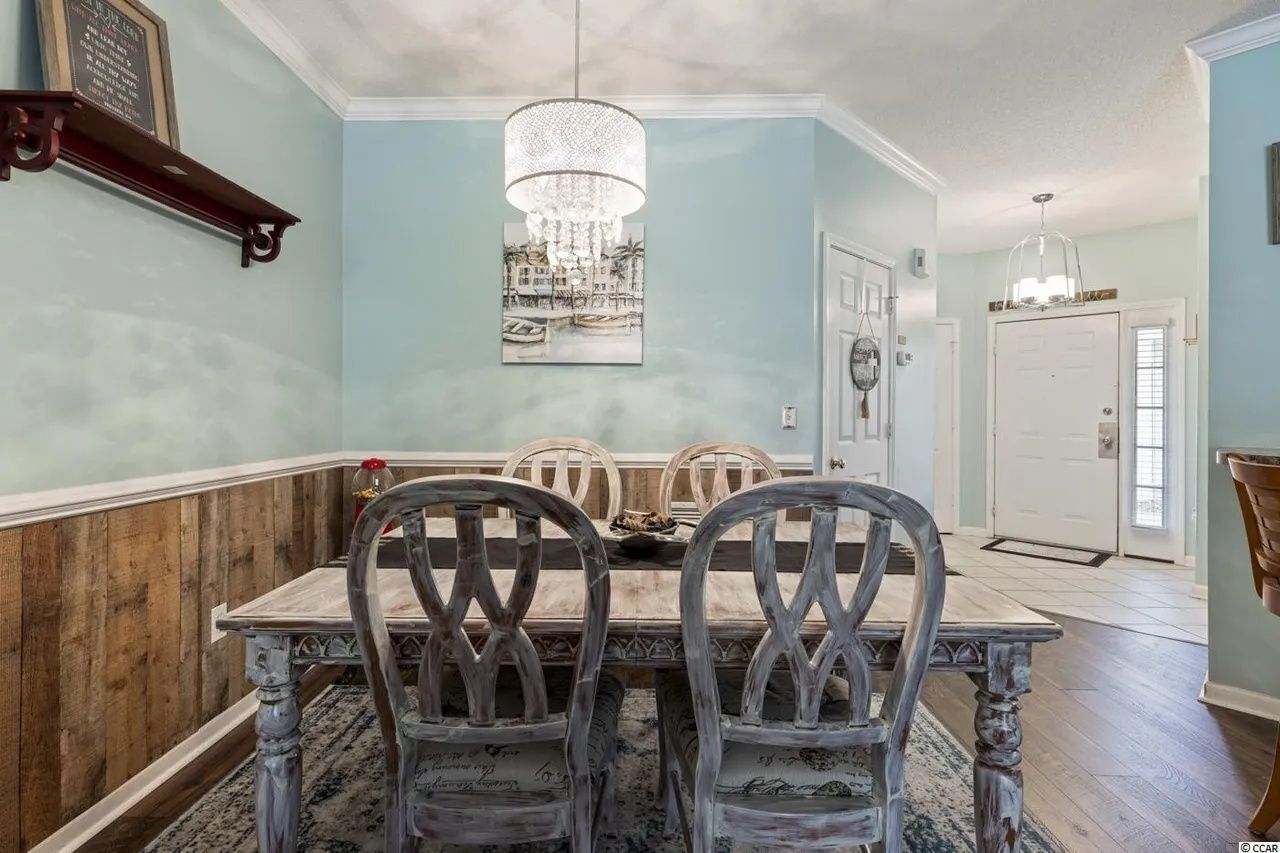 Dining area with a distressed wooden table, chandelier, and entryway in the background.