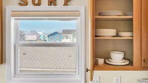 Cucina con vista su case, ripiano con piatti e un cartello con scritto 'SURF' sopra la finestra.