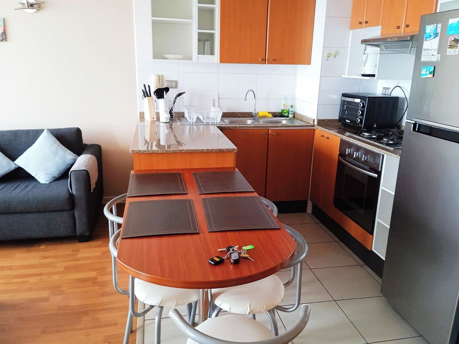 A compact kitchen with a dining area, a sofa, and a refrigerator.