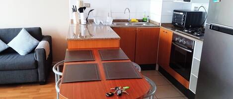 A compact kitchen with a dining area, a sofa, and a refrigerator.