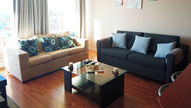 A living room with a beige sofa, a dark sofa, and a glass coffee table. There are two paintings on the wall. - 🛏️ 2 Bedroom Apartment with Panoramic Ocean View 🌊 - Valparaíso (Valparaíso)
