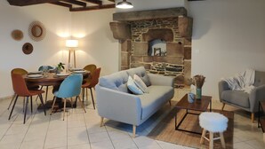 A cozy living room with a stone fireplace, wooden beams, a dining table set for four, and comfortable seating.