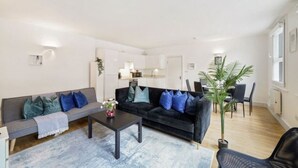 A modern living room with a sofa, a coffee table, and a dining area with chairs. - Trendy 2-Bed, 2-Bath flat near Soho, Marylebone & Oxford Circus (London)