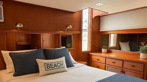 A neatly made bed with a quilted blue blanket and pillows, including one labeled "BEACH". - Luxurious 2-bedroom Yacht in enchanting Puerto Peñasco with AC (Puerto Peñasco)