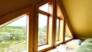 A room with a sloped ceiling and large windows offering a view of a forested landscape.