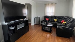 Ein Wohnzimmer mit Flachbildfernseher, einer schwarzen Couch, einem Couchtisch und einem kleinen Beistelltisch.