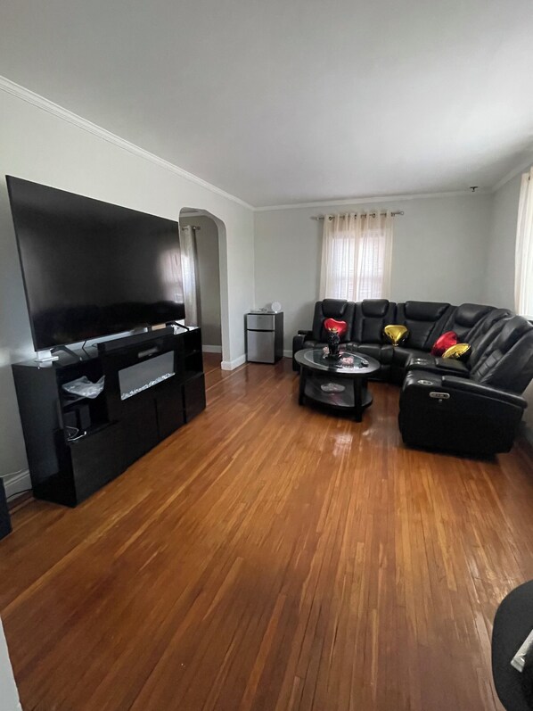 Una sala de estar con televisor de pantalla plana, un sofá negro, una mesa de centro y una mesita auxiliar.