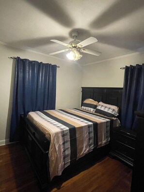 A bedroom with a bed, curtains, a ceiling fan, and a dresser.
