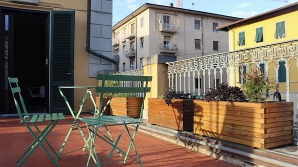 An outdoor seating area with green metal chairs and a wooden planter with plants. - Sonnino Terrace (Pisa)