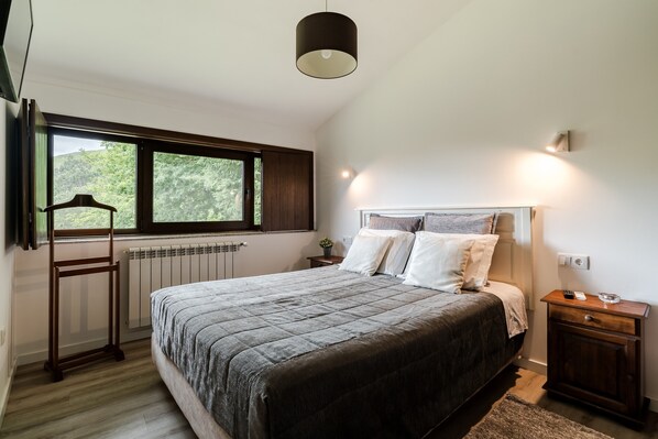 Une chambre à coucher avec un lit, une table de chevet, une lampe, une fenêtre et un radiateur.