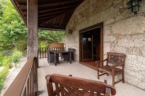 Un edificio de piedra con un balcón de madera, una mesa con sillas y un banco.