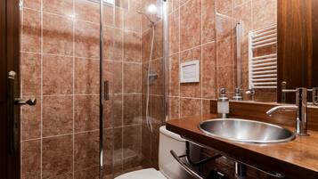 Un baño con ducha de vidrio, inodoro blanco y tocador de madera con lavamanos.