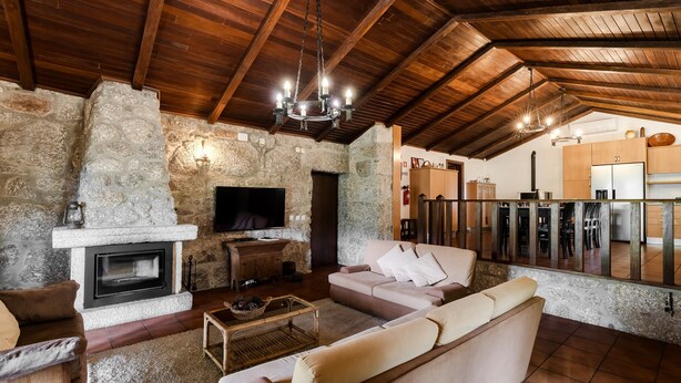 Un interior rústico con chimenea de piedra, vigas de madera en el techo, un sofá y un televisor.