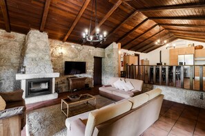 Un intérieur rustique avec une cheminée en pierre, des poutres apparentes en bois au plafond, un canapé et un téléviseur.