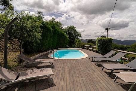 A swimming pool with lounge chairs, surrounded by greenery and a wooden deck.. Villa 'Casa de Férias do Parque da Peneda' with Mountain View, Wi-Fi and Air Conditioning