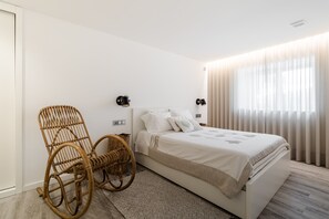 Une chambre à coucher avec un lit, une chaise en osier, une table de chevet et des rideaux.