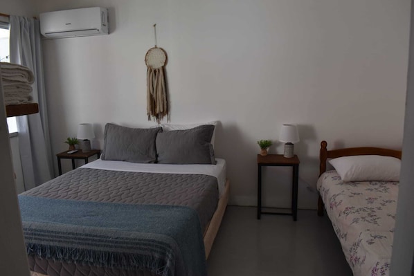A bedroom with a bed, bedside tables, a wall-mounted air conditioner, a dreamcatcher, and a window with curtains. - La casita de Tomi (Colonia del Sacramento)