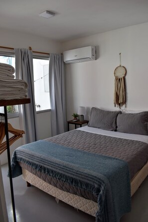 A neatly arranged bedroom with a bed, a bedside table with a lamp, a wall-mounted air conditioner, and a dreamcatcher decoration. - La casita de Tomi (Colonia del Sacramento)