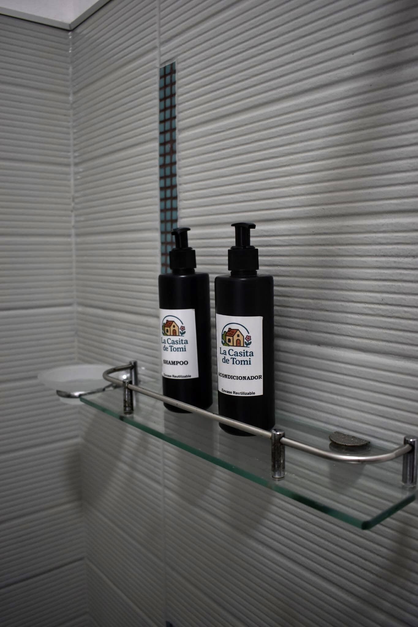 Ein Badezimmer mit einem Glastablett, auf dem sich zwei Flaschen La Casita de Tomi Shampoo und Conditioner befinden.