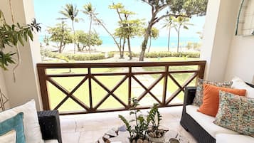 Ein Balkon mit Blick auf den Strand, eine Rattan-Sitzgruppe mit Kissen, ein Holztisch mit Dekoration und ein Geländer.