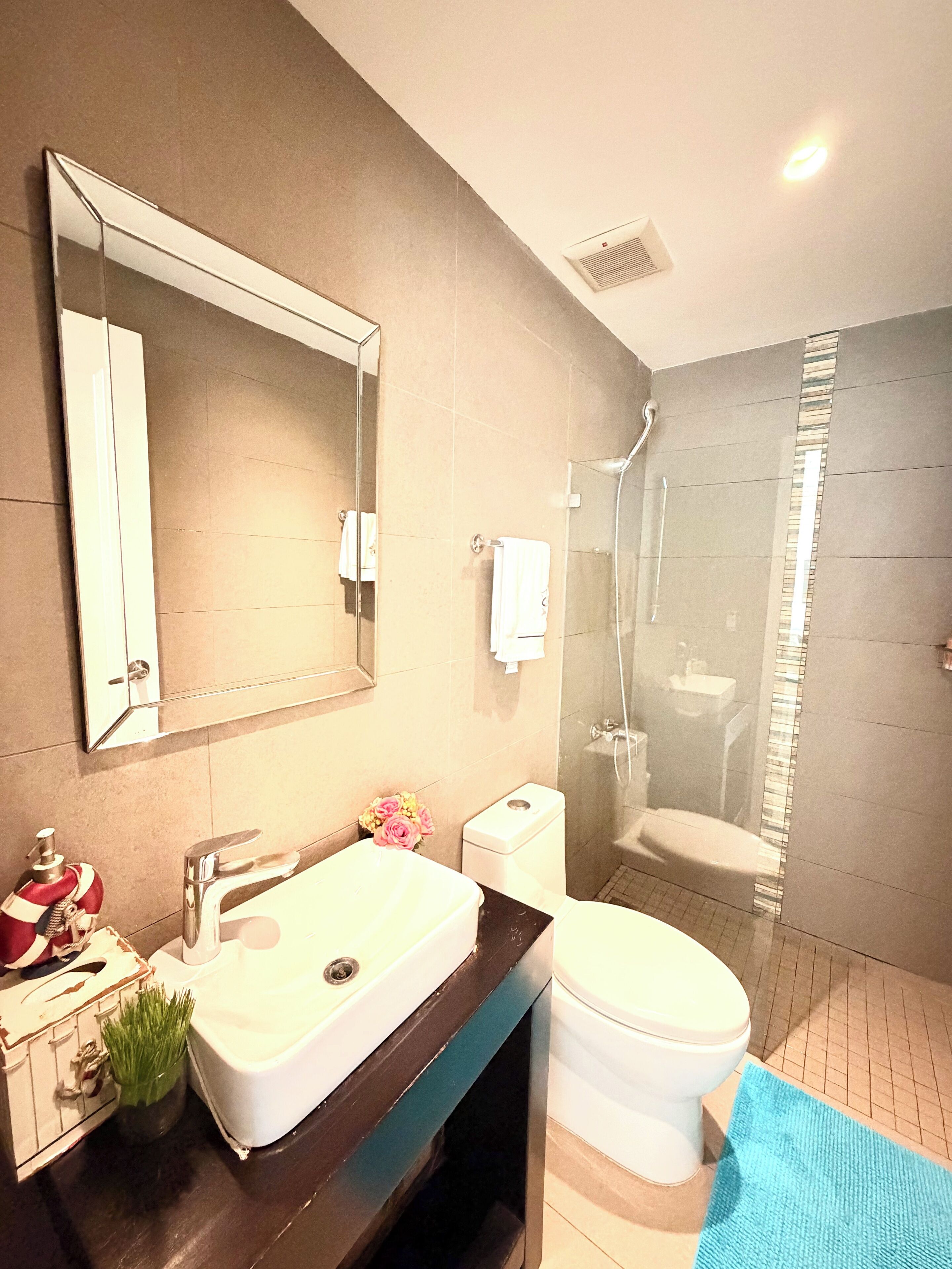 A modern bathroom with a large mirror, a sink, a toilet, and a shower.