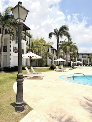 A pool area with lounge chairs, umbrellas, and a lamp post. - Riviera Azul - Playa Dorada (Puerto Plata)