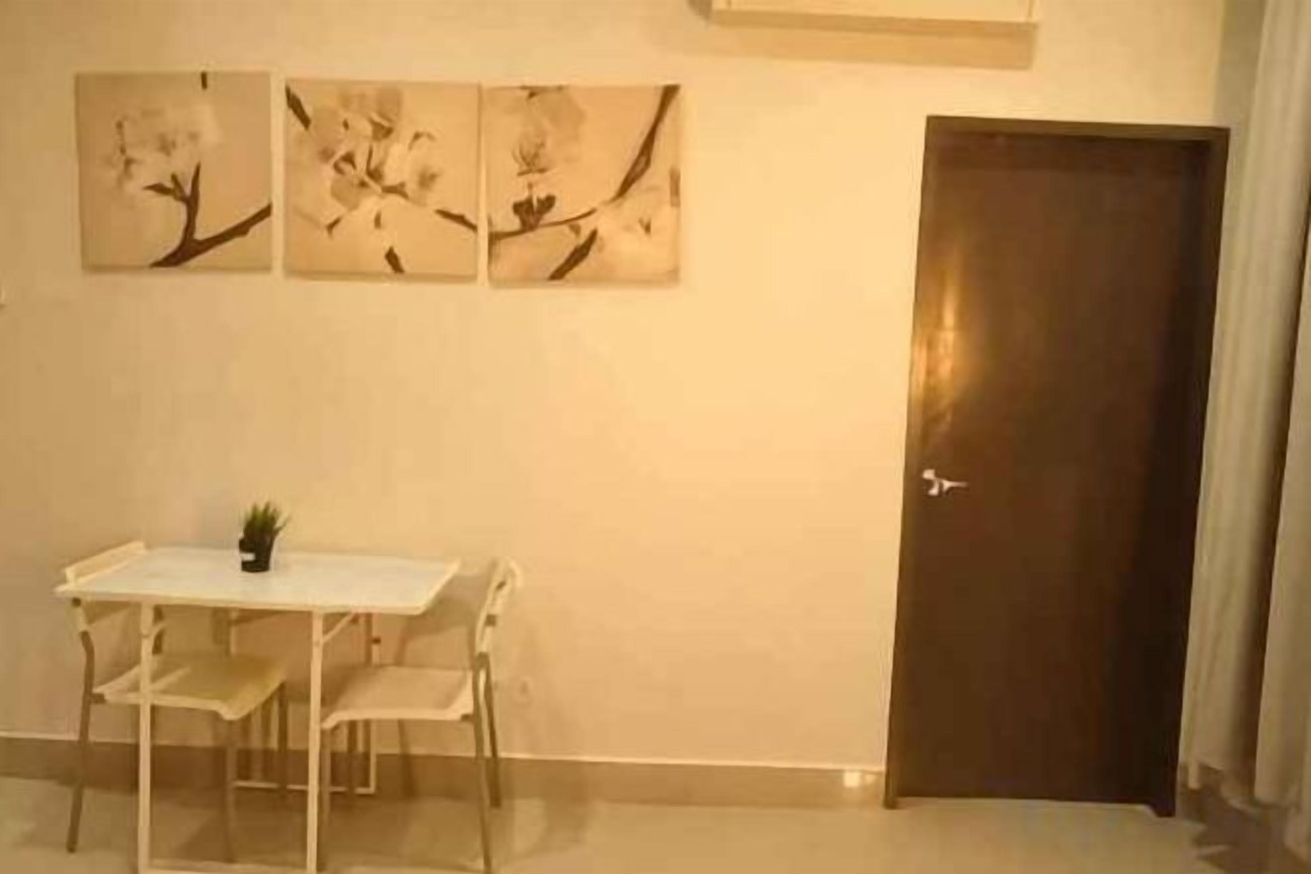 A room with a white table and chairs, a door, and three wall-mounted paintings.