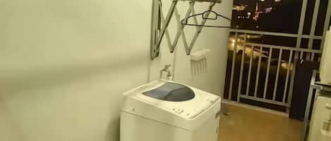 A compact bathroom with a washing machine, a small sink, and a metal railing.