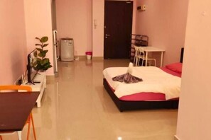 Quarto de hotel com cama, escrivaninha, cadeira, mesinha, lixeira e planta em vaso.