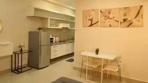 Eine moderne Küche mit Kühlschrank, Mikrowelle und weißen Schränken. Ein kleiner Tisch mit Stühlen und eine Blumenvase sind ebenfalls vorhanden.