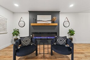 A modern living room with a fireplace, two armchairs, a small table, and decorative plants. - The Reunion House | St Charles 4BR Sleeps 14 Game Room Hot Tub | Mercer Stays (Saint Charles)