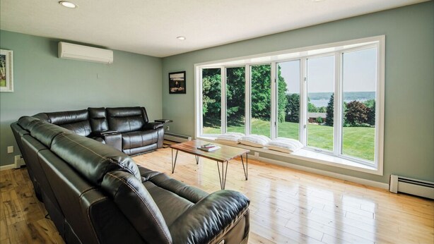 A spacious living room with a leather sofa, a coffee table, and large windows offering a view of a garden and a body of water.