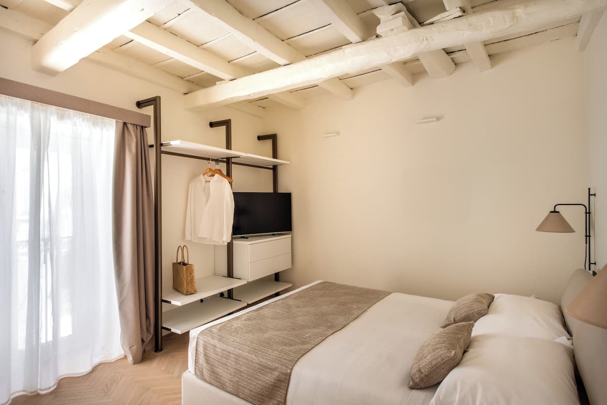 A bedroom with a bed, a TV, a shelf with a bag, and a lamp.
