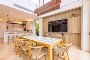 A modern kitchen with a dining area, wooden furniture, and a large TV.