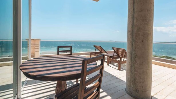 Een balkon met een tafel en stoelen, met uitzicht op een wateroppervlak.