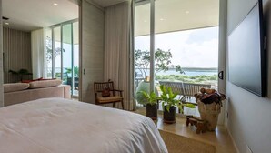 A modern hotel room with a large bed, a balcony with a view, and a television mounted on the wall.